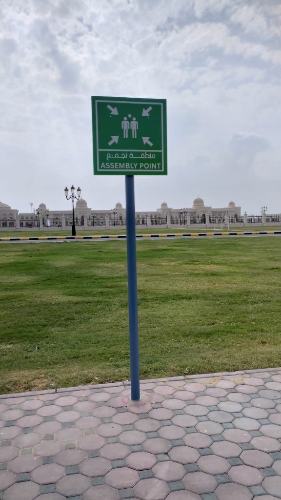 Installed green bilingual ASSEMBLY POINT sign outdoors
